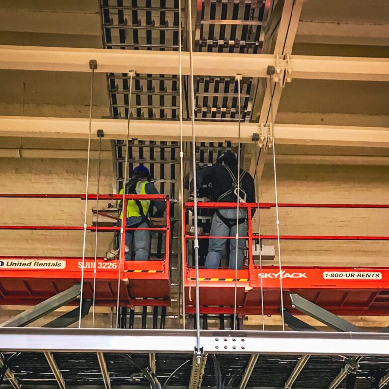 Two workers using skyjacks to reach ceiling pipes
