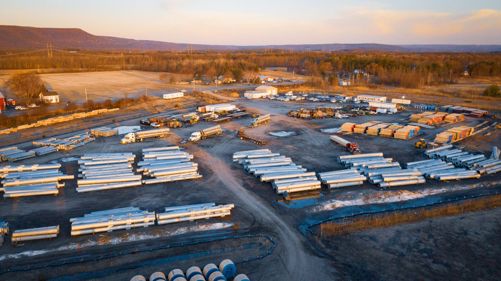 Large field with stacks of large pipes, small buildings and trucks