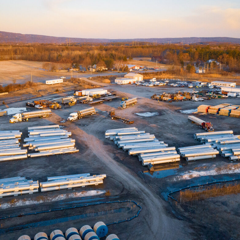 Large field with stacks of large pipes, small buildings and trucks