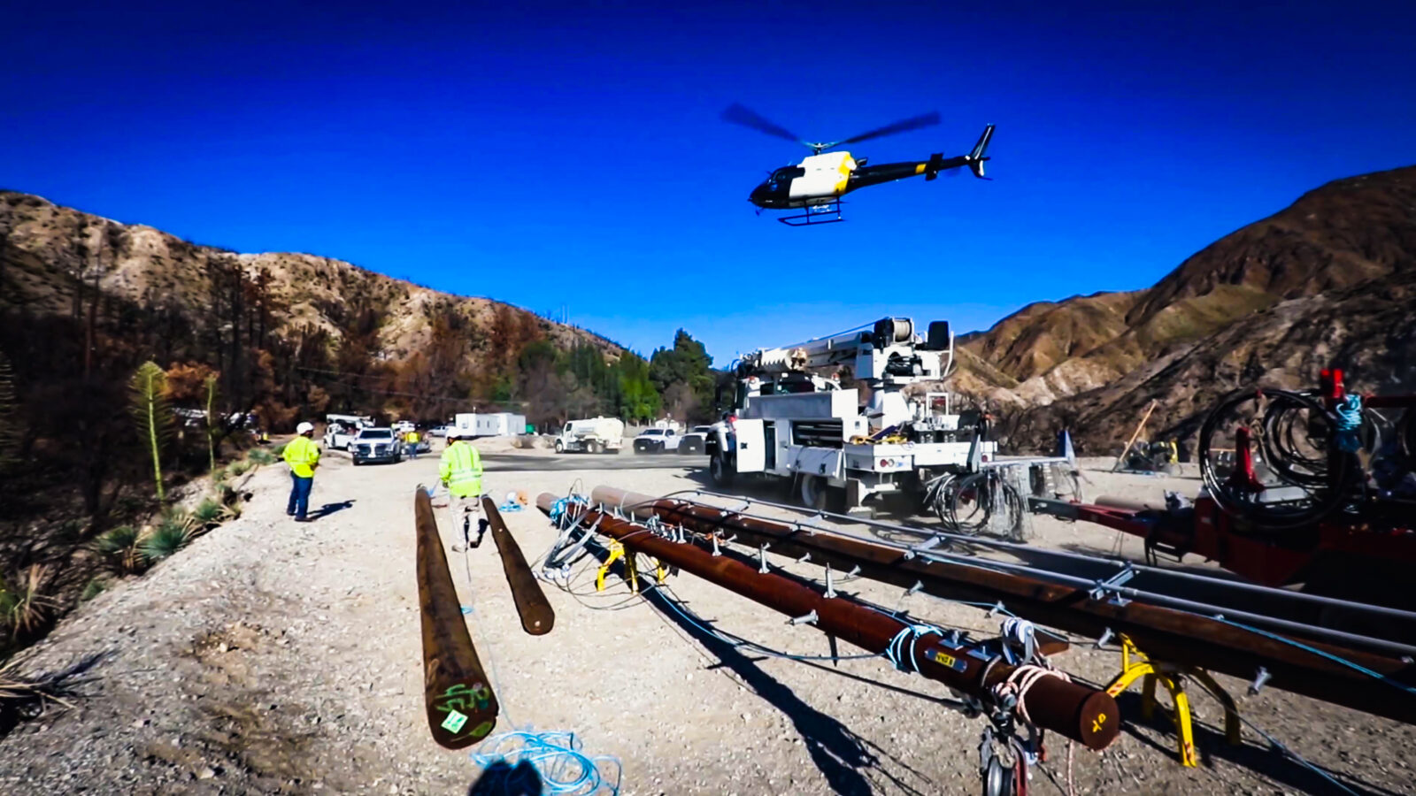 Row of power line poles with a white bucket truck and helicopter