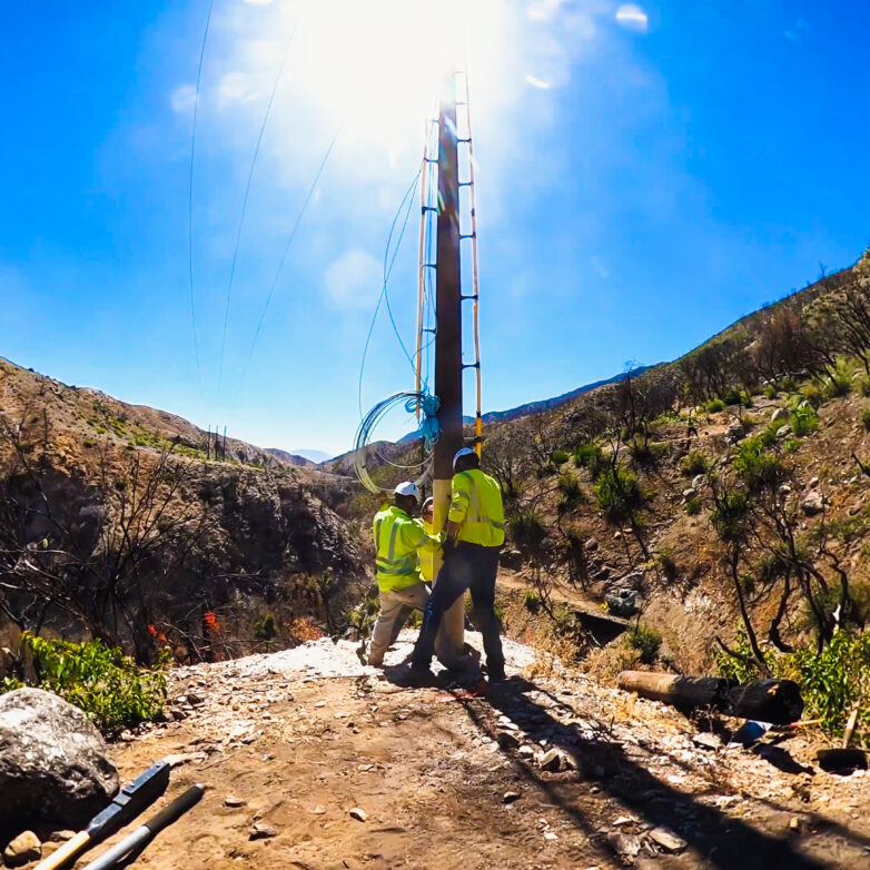 Two Harlan Electric workers placing a power line pole correctly into the ground