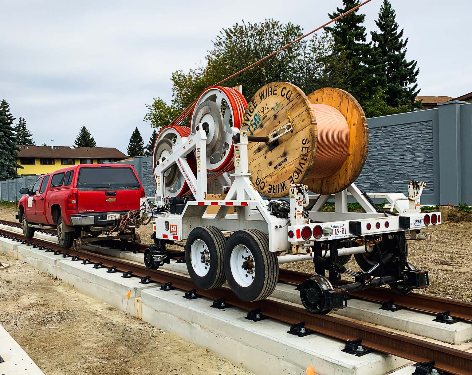 Red truck with a trailer of power wires on a railway