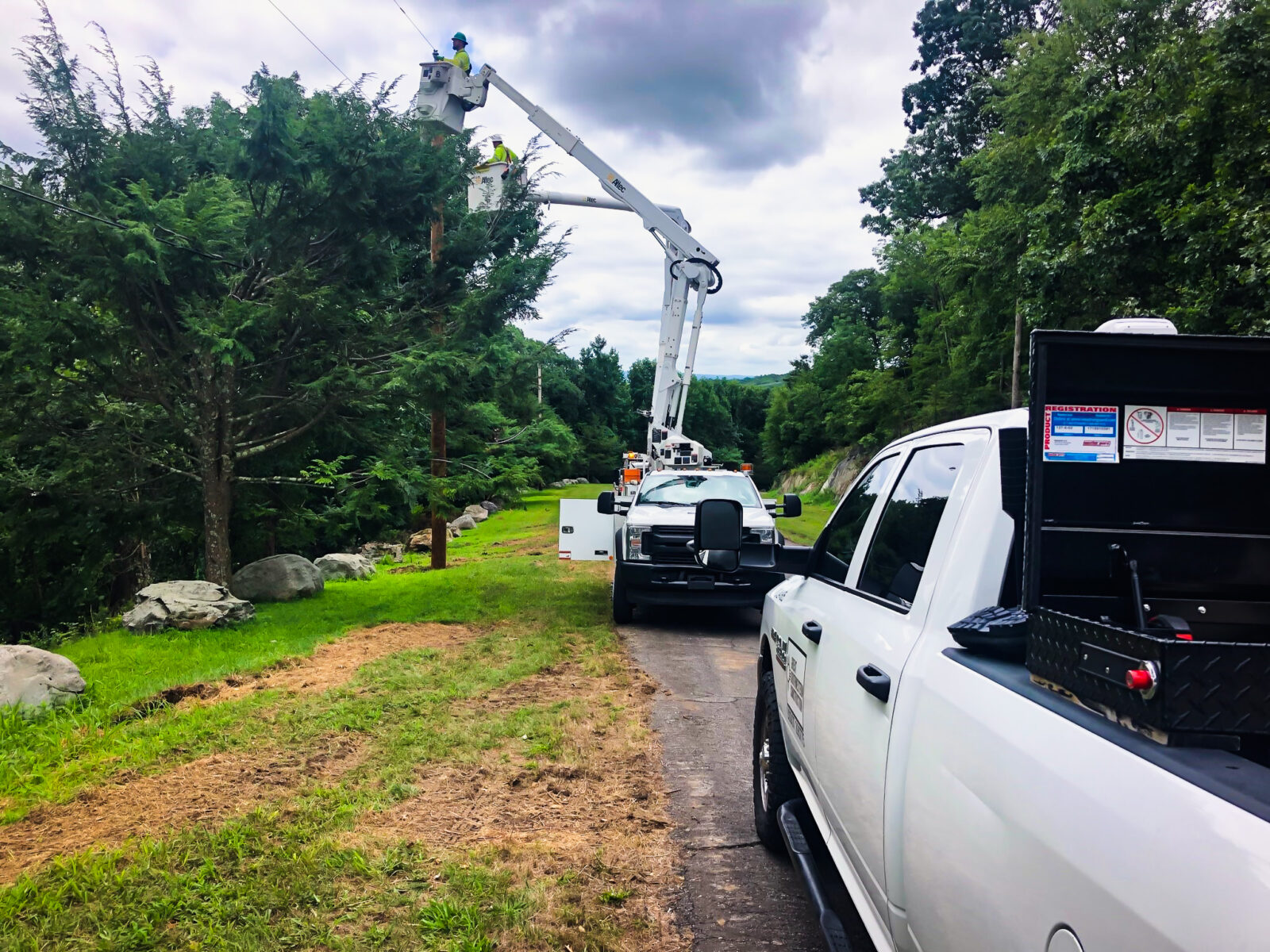 Two L.E. Myers vehicles in right of way with employee in bucket repairing transmission lines
