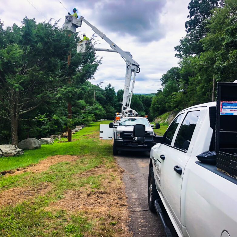 Two L.E. Myers vehicles in right of way with employee in bucket repairing transmission lines