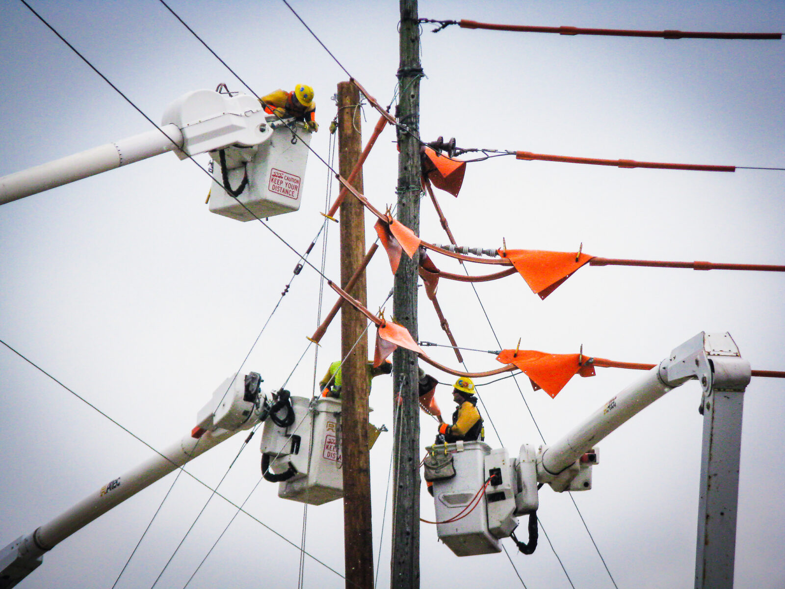 Workers on elevated platforms placing safety covers on power lines
