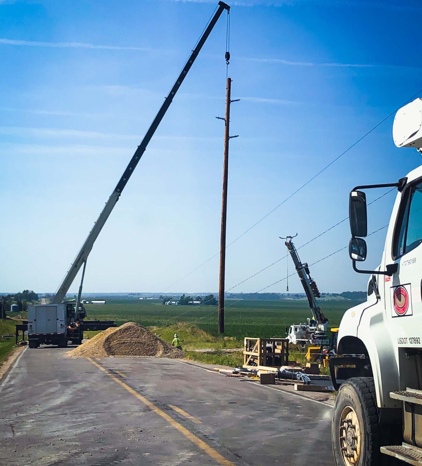 White truck with crane placing a power line pole on to the ground