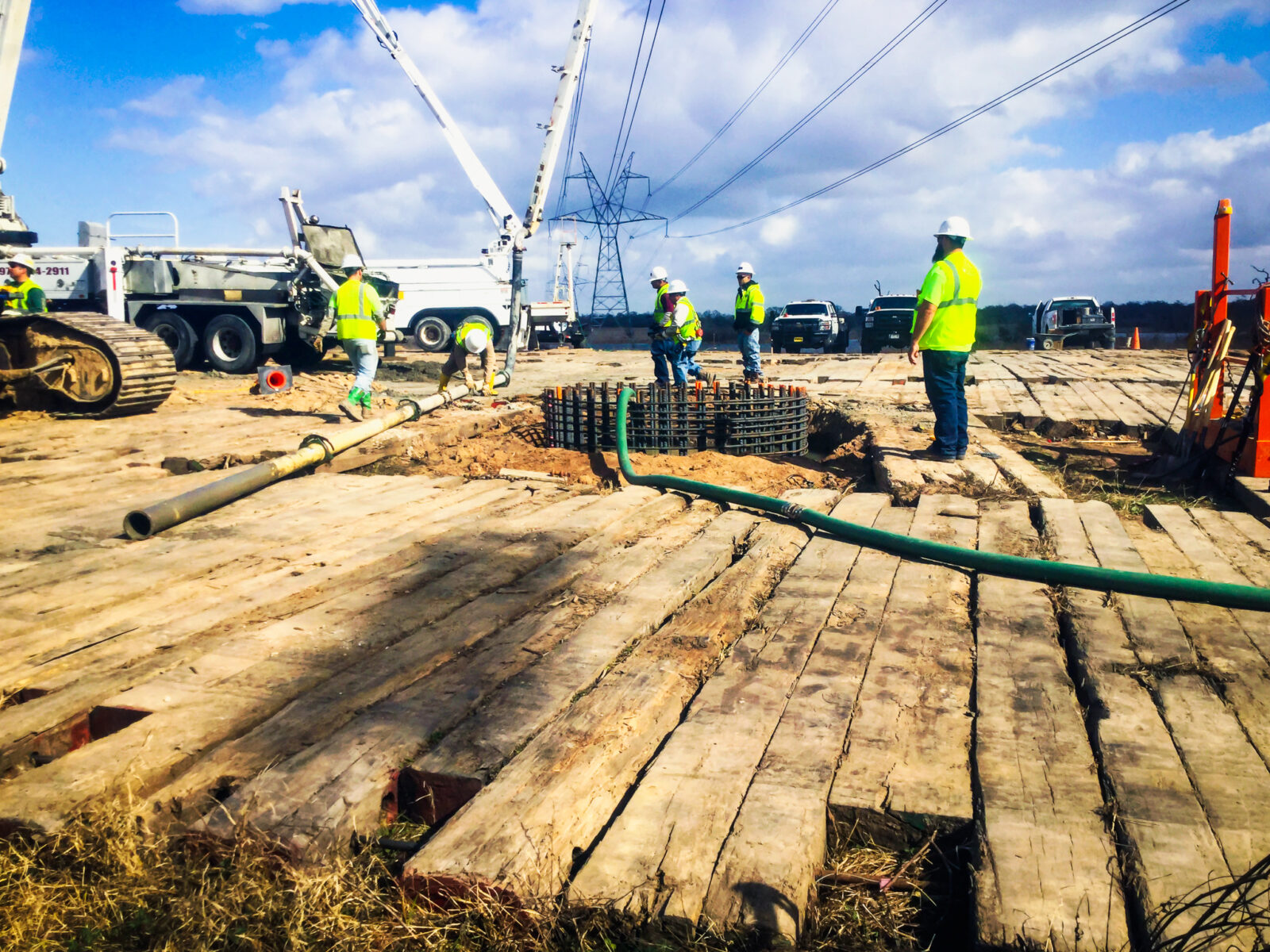 L.E. Myers employees working on transmission line install with fleet of trucks in the background