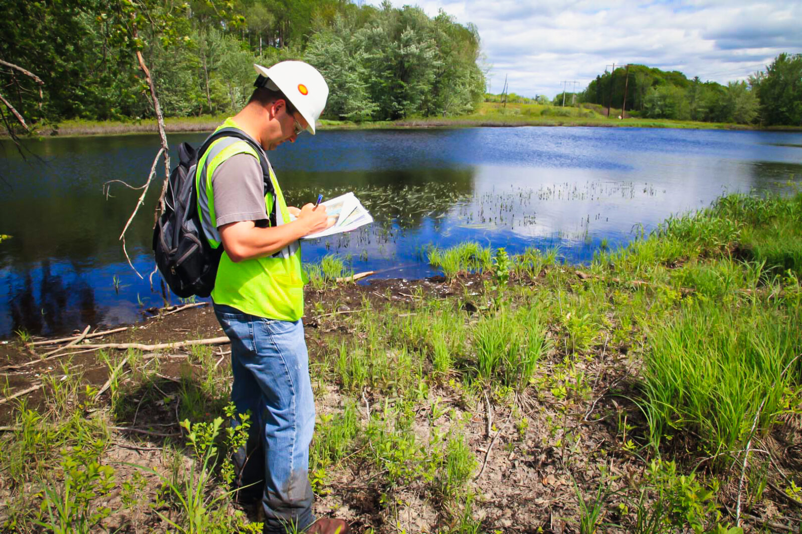 MYR Group employee with a backpack reviews his notes alongside a lake