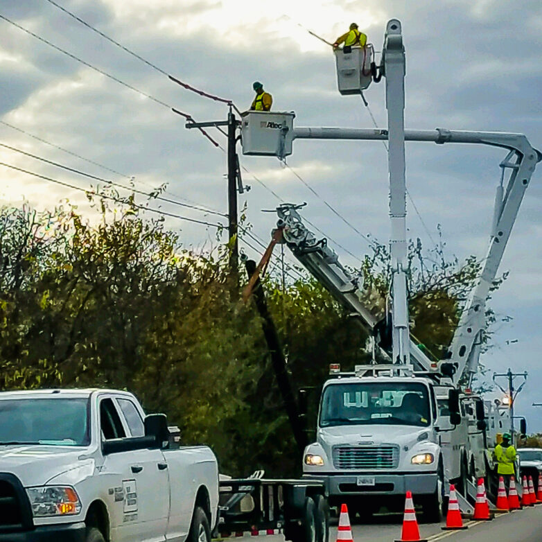 Restoration workers on bucket trucks beside a power line