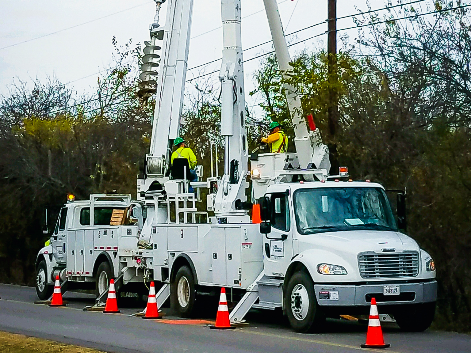 Two restoration workers on two white bucket trucks
