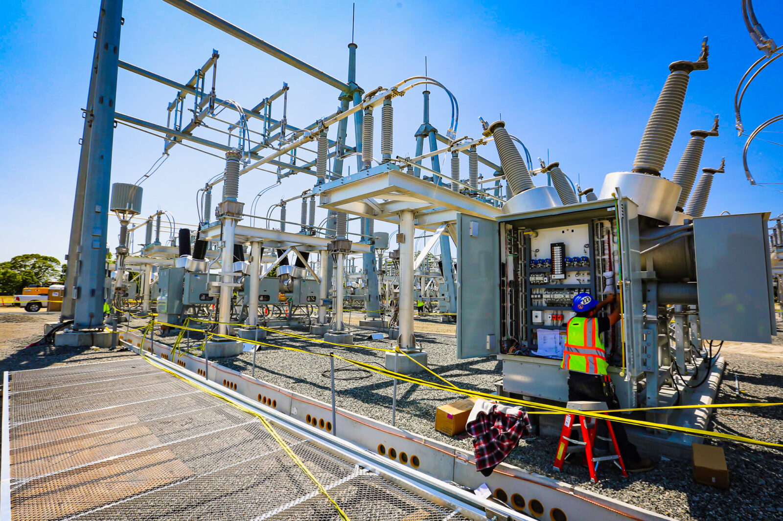 Worker in safety gear working on substation with blue skies