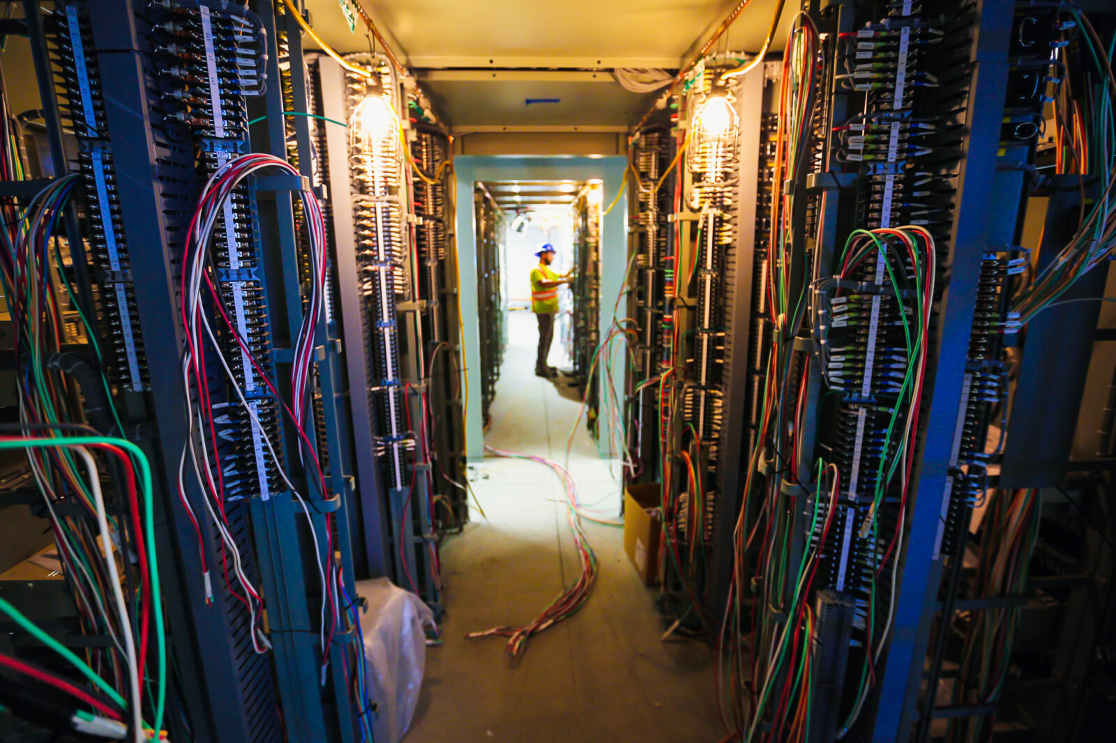 Red and blue wires line a hallway in the substation while a crew member works on a project in the distance