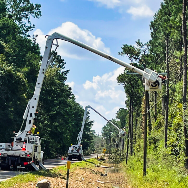 Two white bucket trucks parked on a road with buckets elevated beside power lines