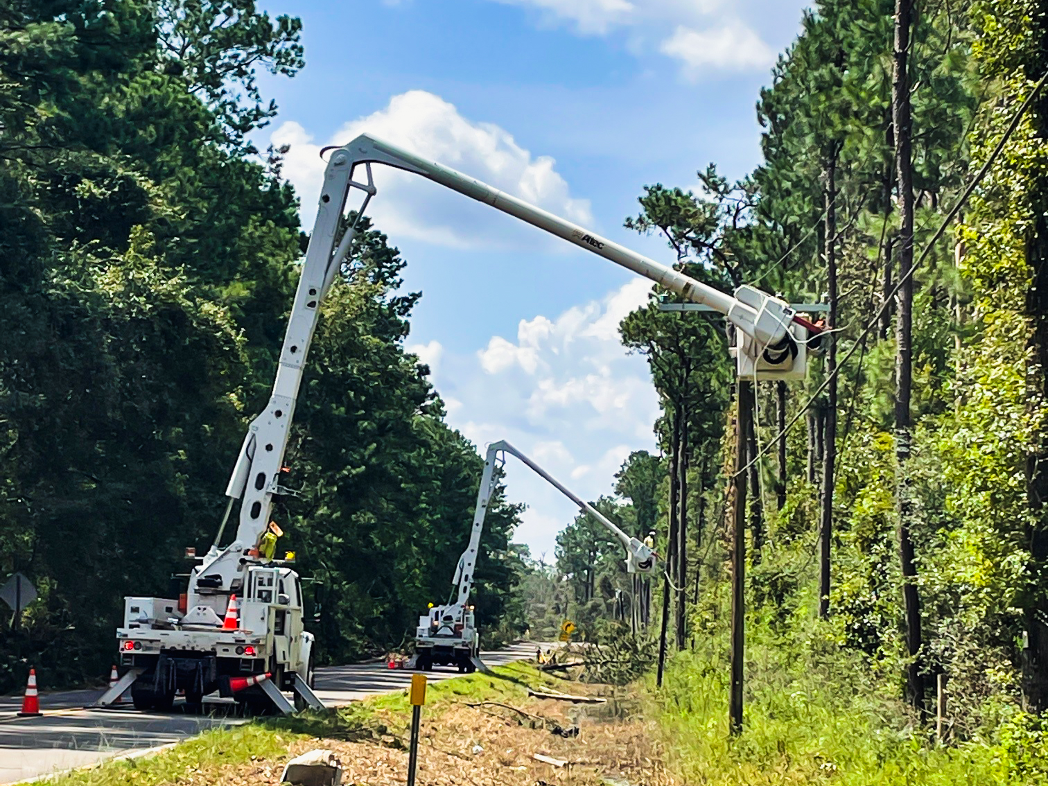 Two white bucket trucks parked on a road with buckets elevated beside power lines