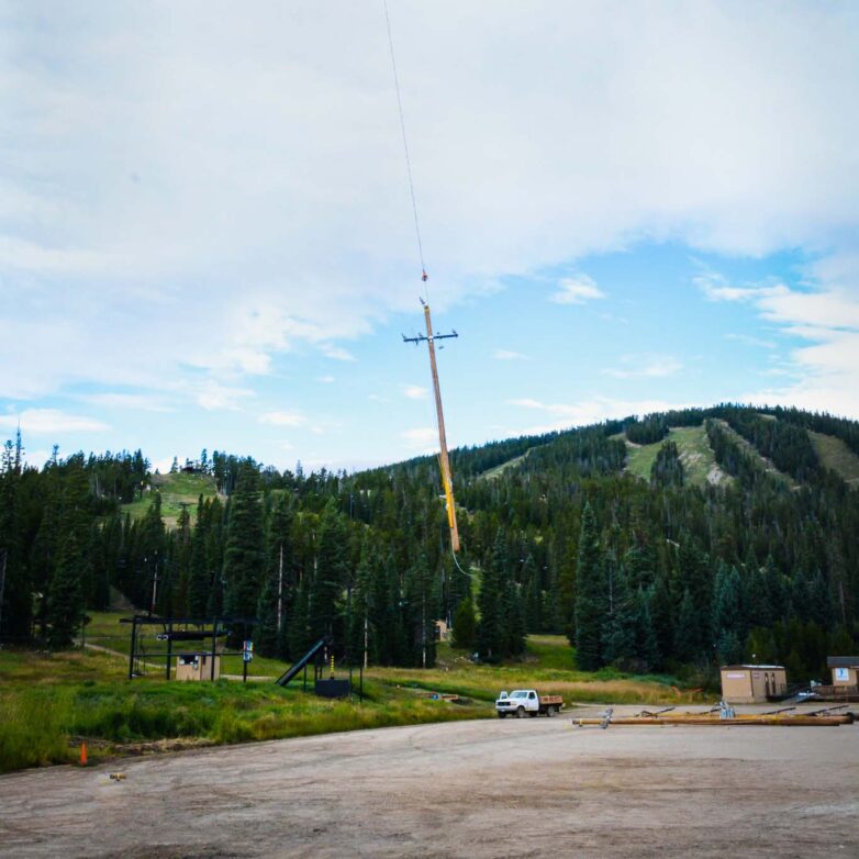 An wood distribution pole is flown through the air over a gravel lot.