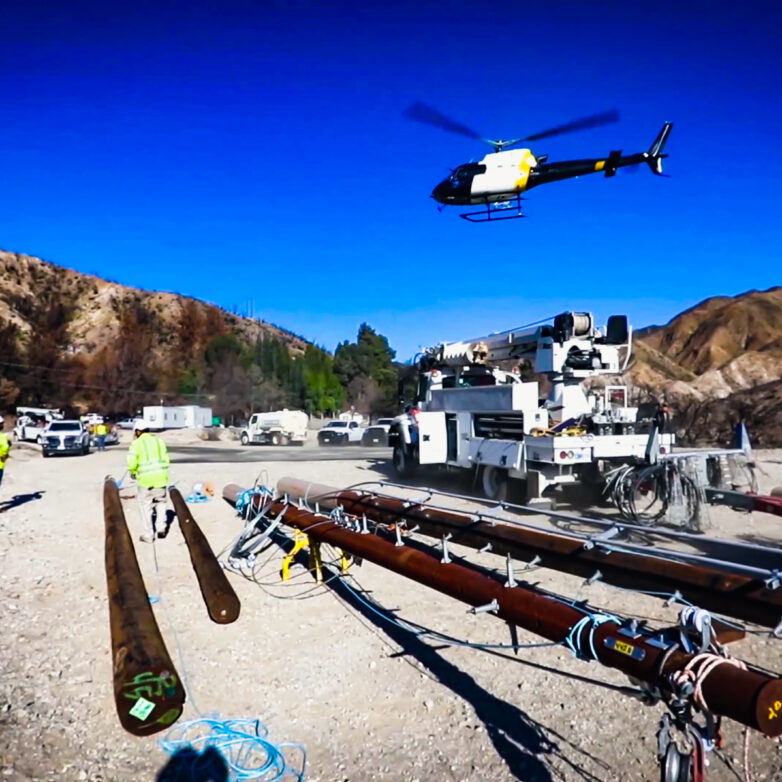 A helicopter flies above an area where power poles lay on the ground waiting for installation in California.