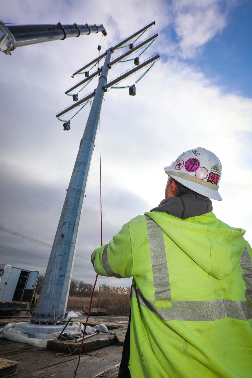 An electrical lineworker holds a rope below a steel structure.