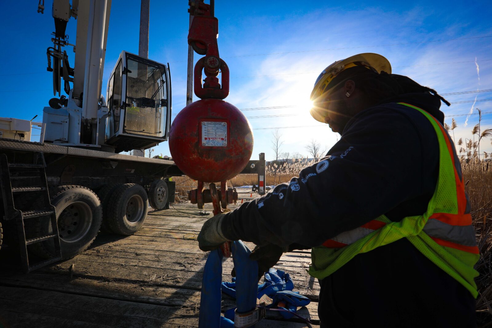 An electrical lineworker holds a pulley next to a crane truck.