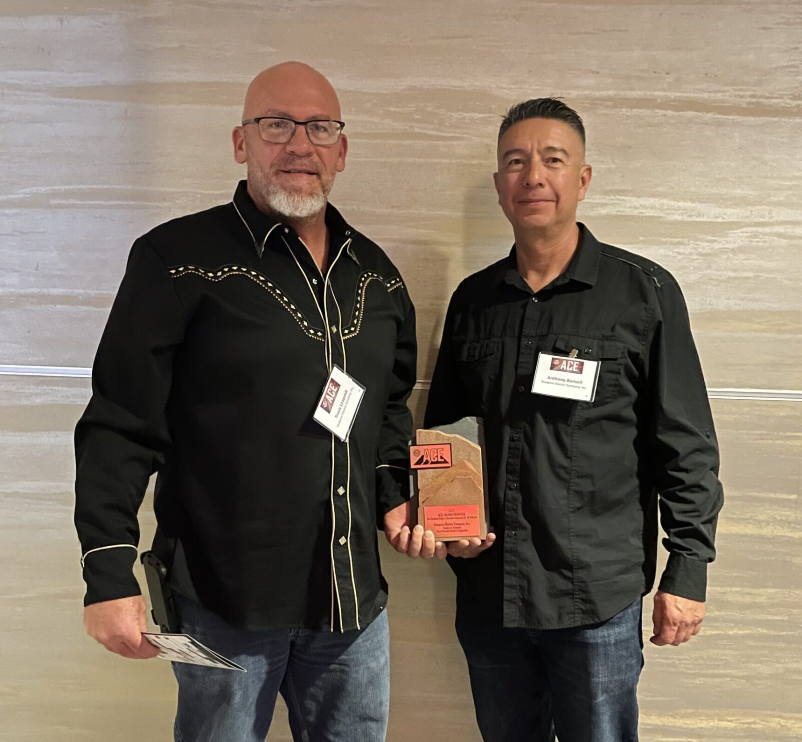 Two men in black shirts and jeans hold an award