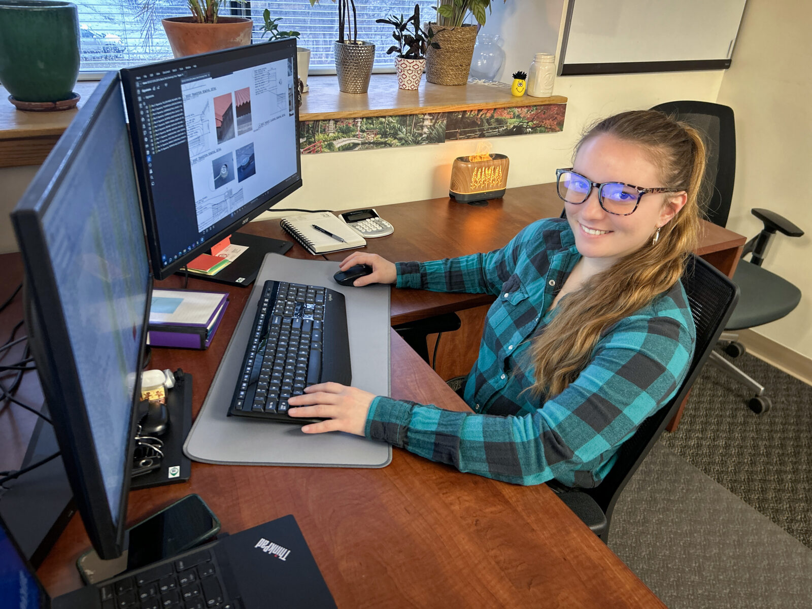 Female construction administrative employee sits at a desk in front of computers.