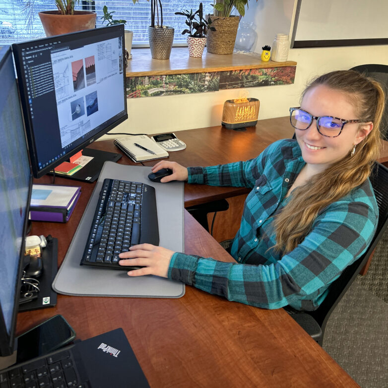 Female construction administrative employee sits at a desk in front of computers.