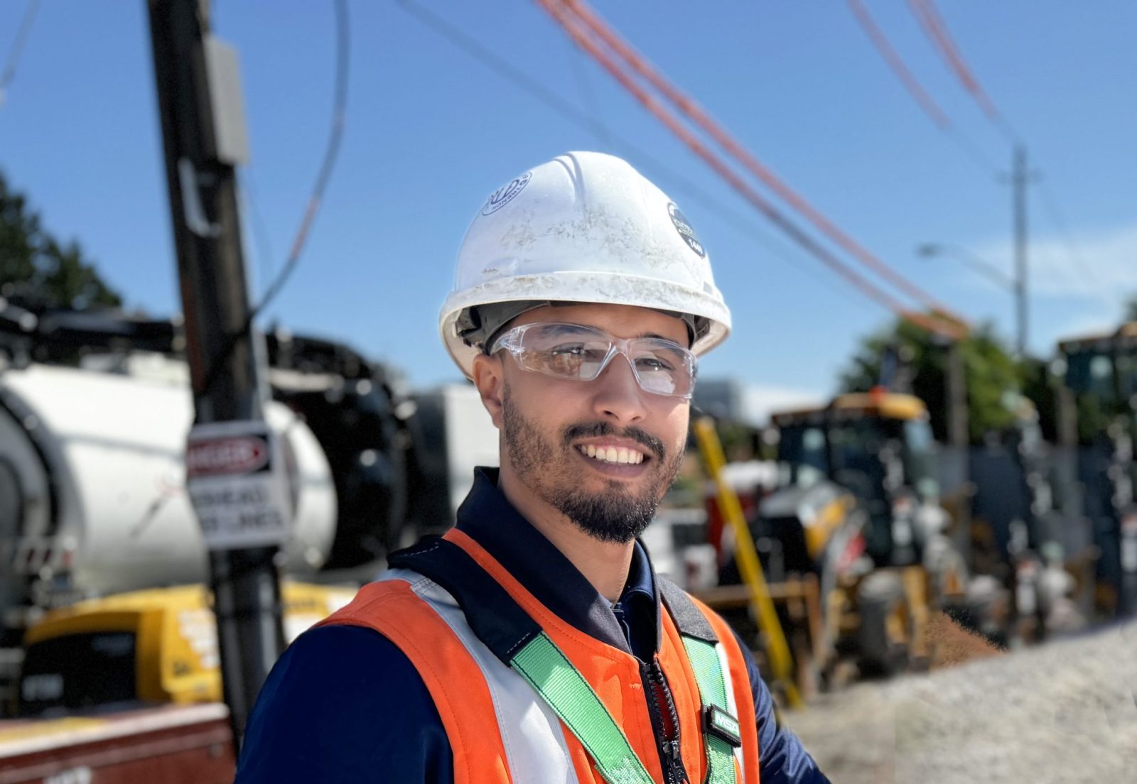 A construction manager in a hard hat, gloves, and protective glasses stands over a blueprint