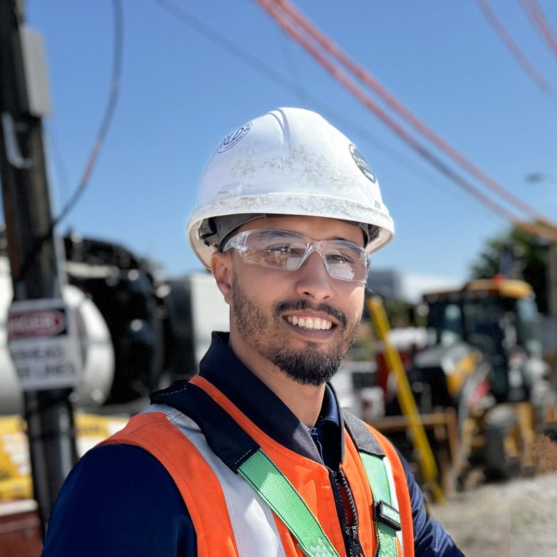 A construction manager in a hard hat, gloves, and protective glasses stands over a blueprint