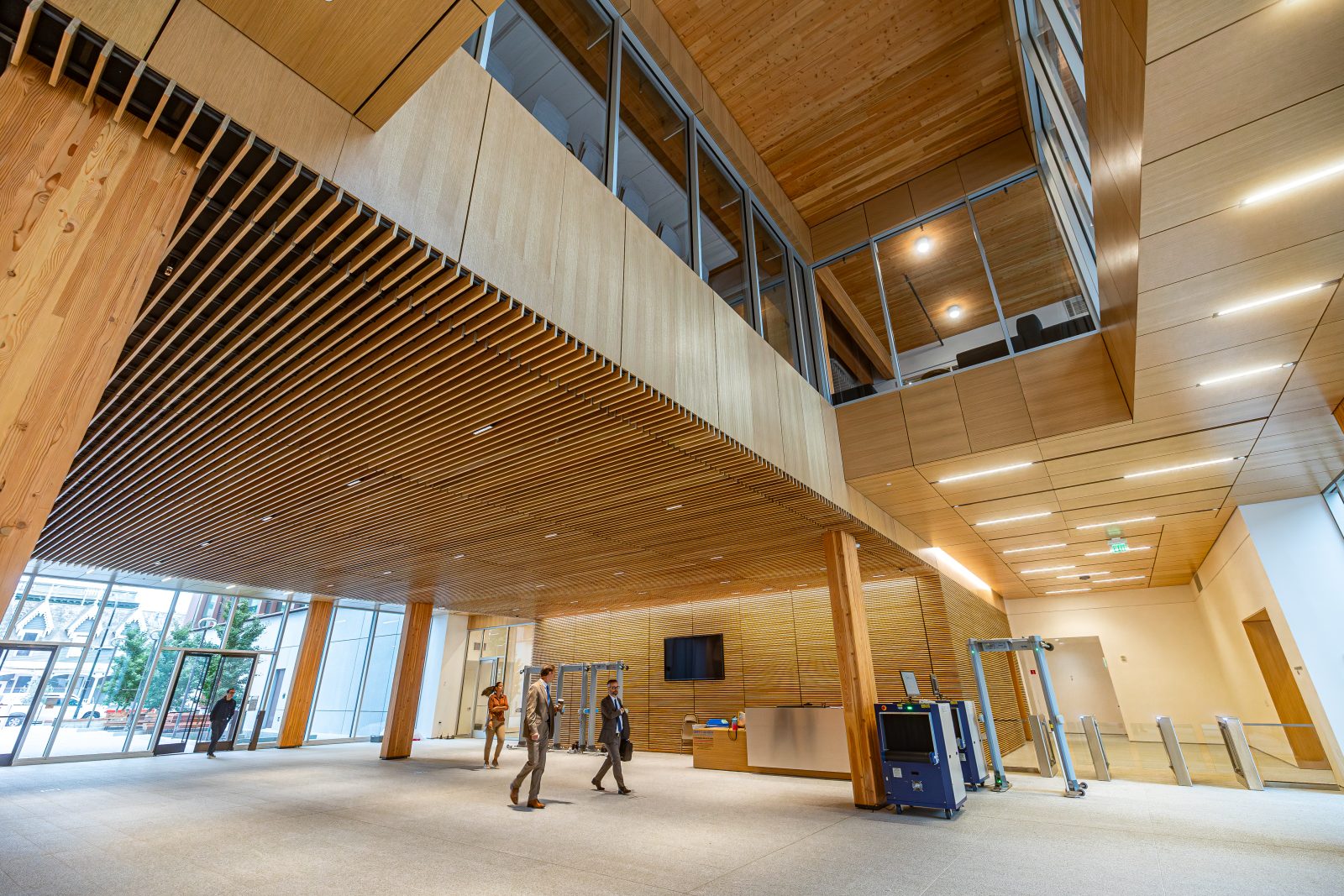 people walking inside a building with lots of wood and glass