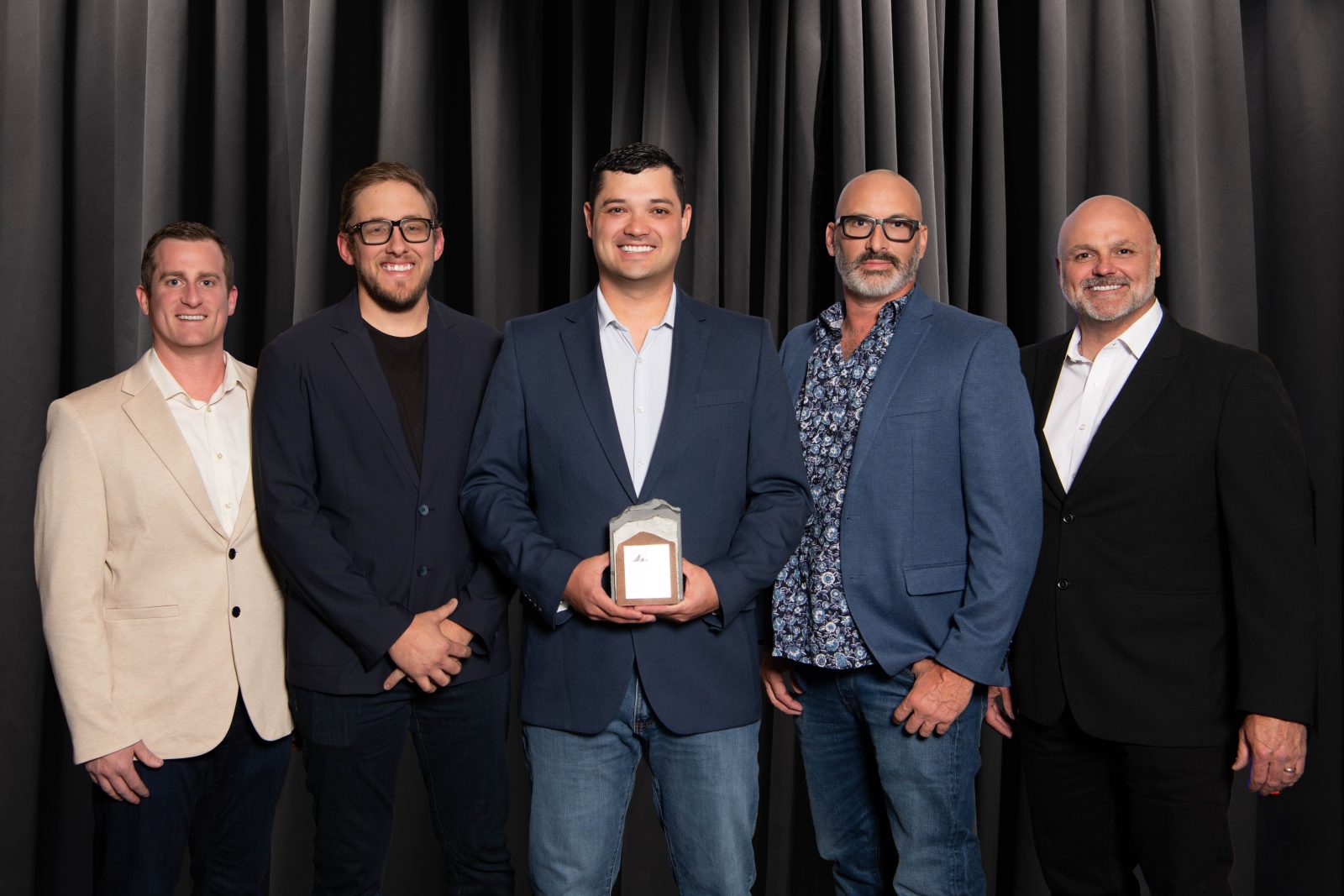 Five men dressed in suits stand together holding a trophy